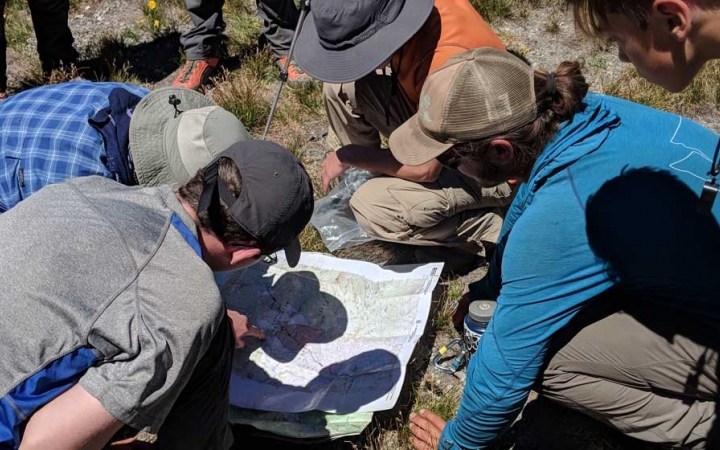 students gather around a map on the ground during a backpacking course with outward bound